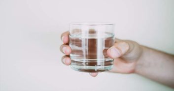 Verre d’eau tenu à la main, symbole du jeûne hydrique et de détox / Description : main qui tient un verre d'eau pour le jeûne hydrique suivi d'une cure de sève de bouleau Probiotisève